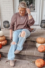 woman wearing a mauve oversized sweater and distressed light blue jeans, sitting on steps surrounded by pumpkins