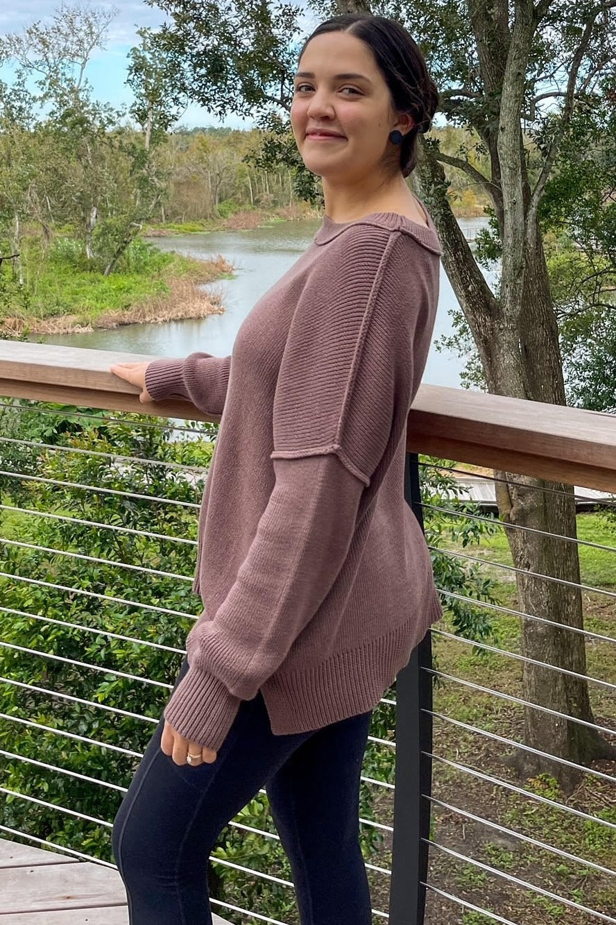 woman wearing a mauve oversized sweater with ribbed detailing and black leggings, standing outdoors by a lake