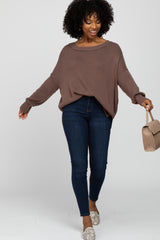 woman wearing a brown oversized knit sweater and dark skinny jeans, holding a beige handbag