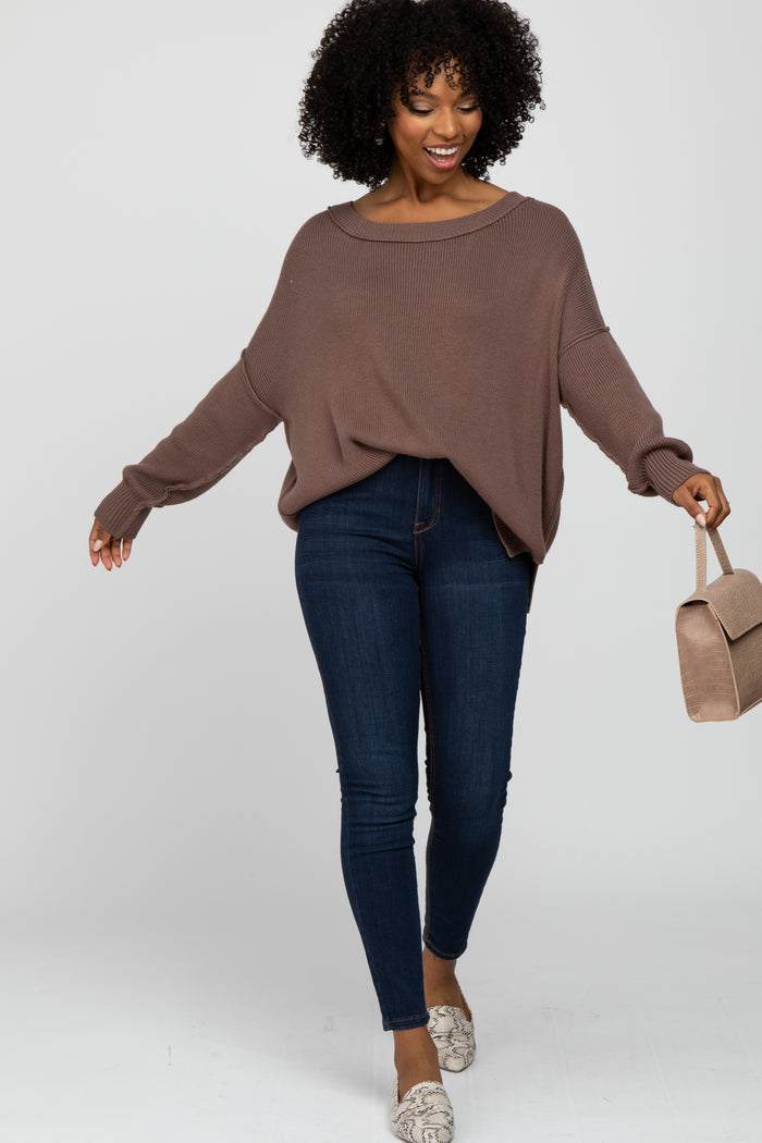woman wearing a brown oversized knit sweater and dark skinny jeans, holding a beige handbag