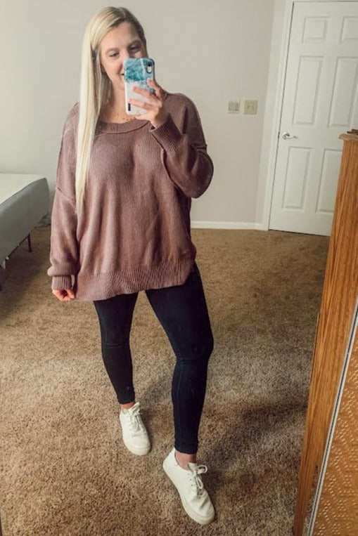woman wearing a mauve oversized sweater, black skinny jeans, and white sneakers, taking a mirror selfie