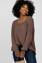 woman wearing a loose brown ribbed sweater and dark jeans, smiling while holding a small handbag