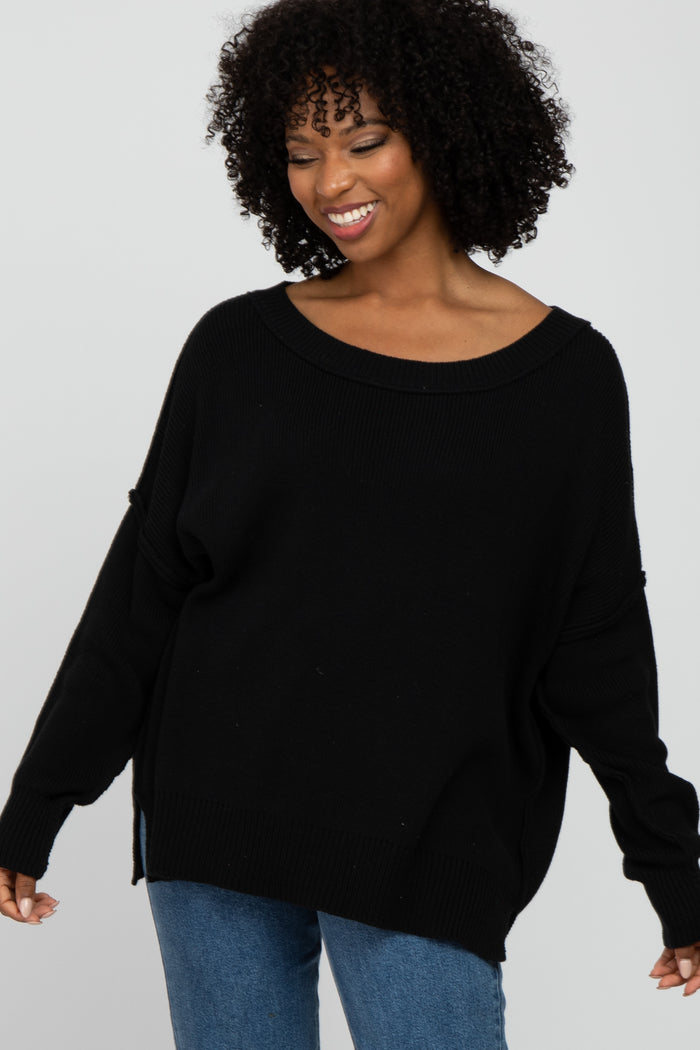 smiling woman with curly hair wearing a black oversized knit sweater and blue jeans