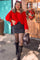 woman wearing a red oversized sweater with a black denim mini skirt and knee-high black boots