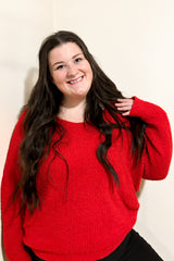 woman wearing a vibrant red oversized sweater with long sleeves and smiling at the camera