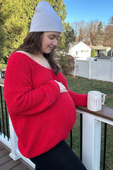 woman wearing a red oversized maternity sweater and holding a mug while showcasing her baby bump