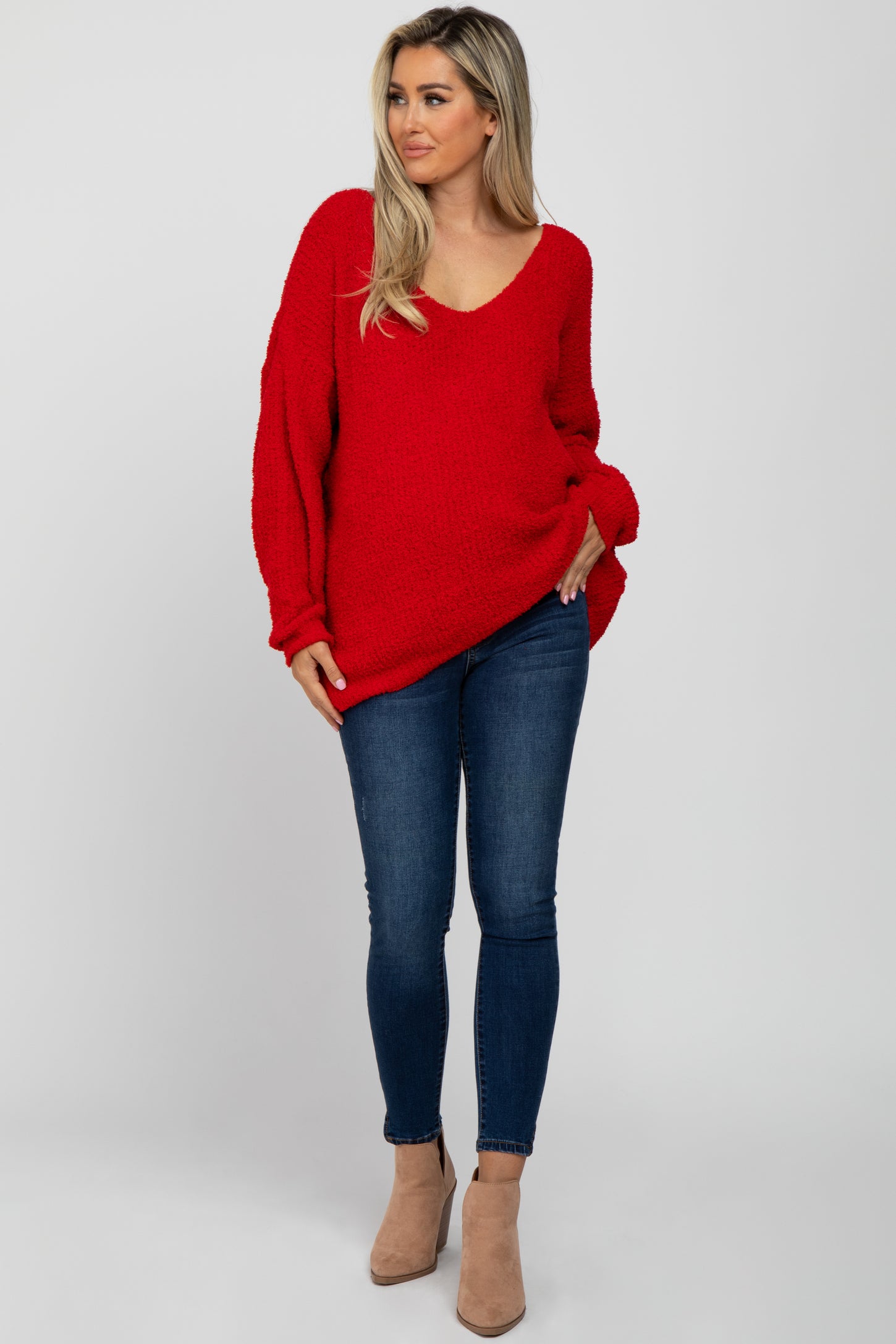 woman wearing a red oversized maternity sweater and blue skinny jeans, with her hands in the pockets