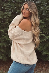 woman wearing a cream off-the-shoulder oversized sweater with long sleeves and blue jeans