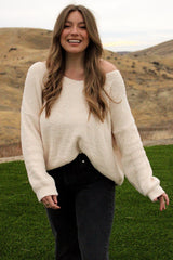 woman wearing an off-white oversized sweater with a relaxed fit and long sleeves, paired with black jeans, smiling outdoors