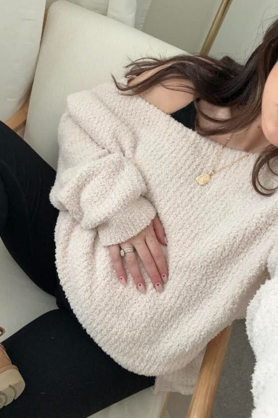 woman wearing a soft pink off-the-shoulder maternity sweater, holding her baby bump while seated