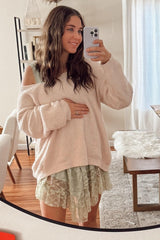 woman wearing a light pink oversized maternity sweater and a green lace dress, holding her baby bump in the mirror selfie