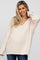 smiling woman wearing a cream oversized v-neck fuzzy knit sweater and blue jeans
