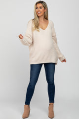 woman wearing a light beige oversized maternity sweater with a v-neck and distressed blue maternity jeans, showing her baby bump