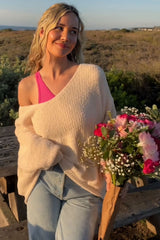 woman wearing a soft beige oversized sweater and light blue high-waisted jeans, holding a bouquet of flowers