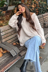woman sitting on a bench wearing a beige oversized sweater and light blue flared jeans with black ankle boots
