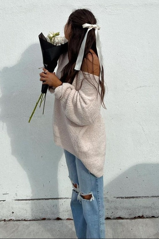 woman wearing a soft pink oversized sweater and ripped light blue jeans, holding a bouquet of white flowers