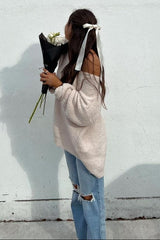 woman wearing a soft pink oversized sweater and ripped light blue jeans, holding a bouquet of white flowers