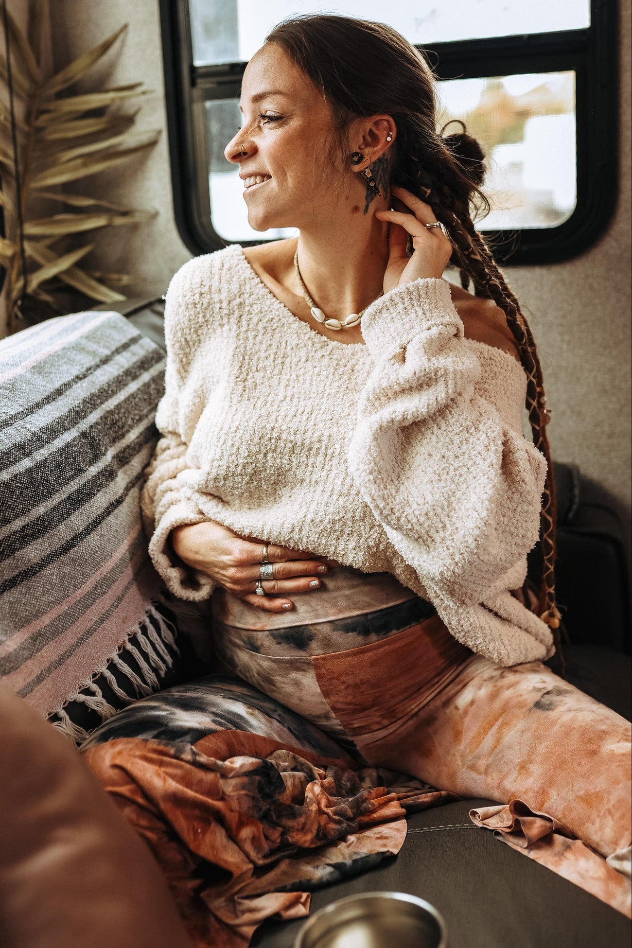 woman wearing a cream oversized sweater and colorful tie-dye maternity leggings, sitting and showing her baby bump