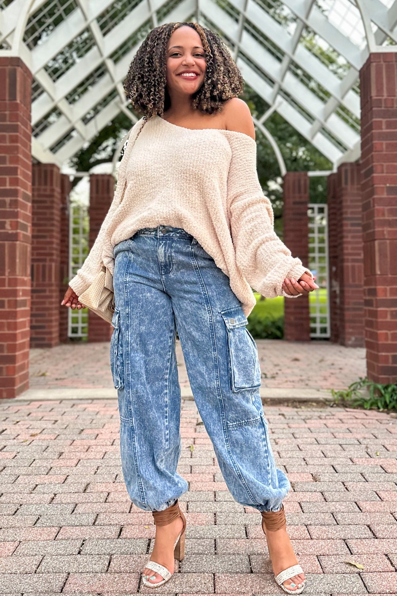 woman wearing a cream oversized off-the-shoulder sweater and light blue cargo jeans with side pockets and heeled sandals