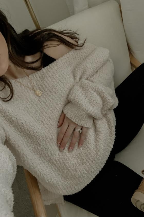 woman wearing a cream oversized maternity sweater with an off-shoulder style while resting her hand on her baby bump