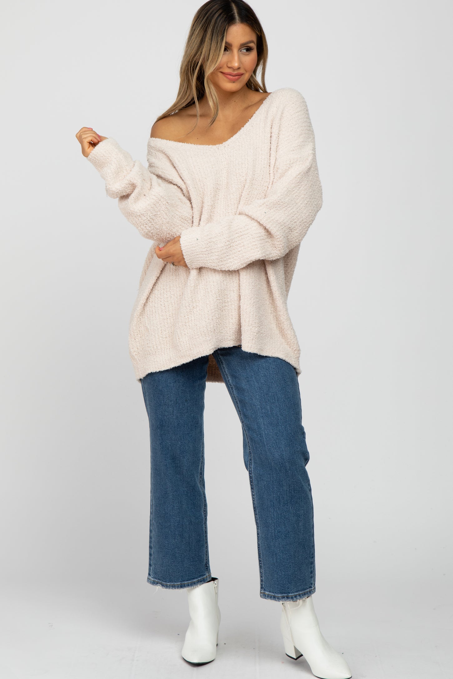 woman wearing a soft pink oversized sweater with an off-the-shoulder style and paired with blue wide-leg jeans and white ankle boots