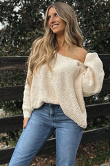 woman wearing a cream off-shoulder chunky knit sweater and blue high-waisted jeans, smiling outdoors