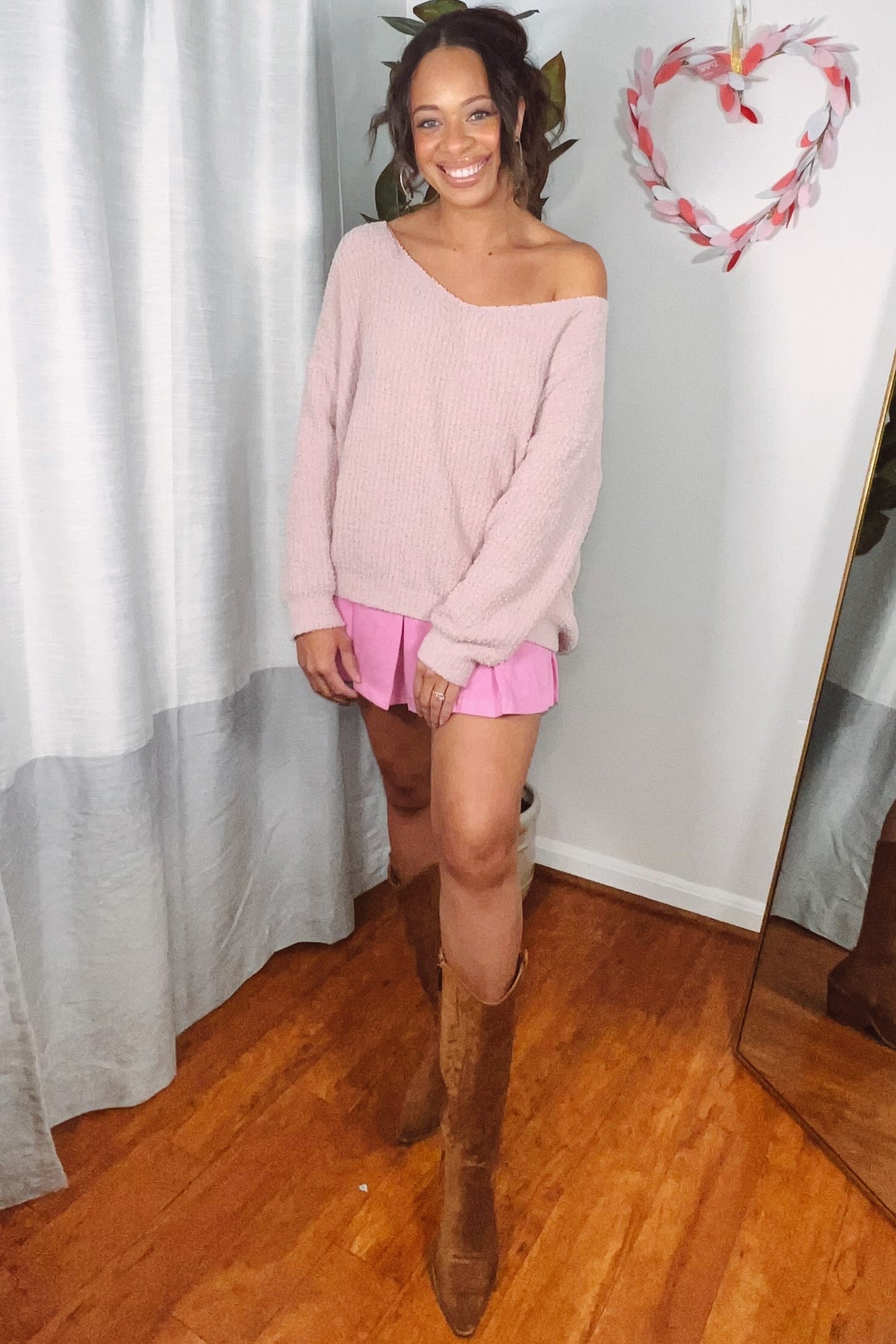 woman wearing a soft pink off-the-shoulder sweater with pink shorts and tall brown boots