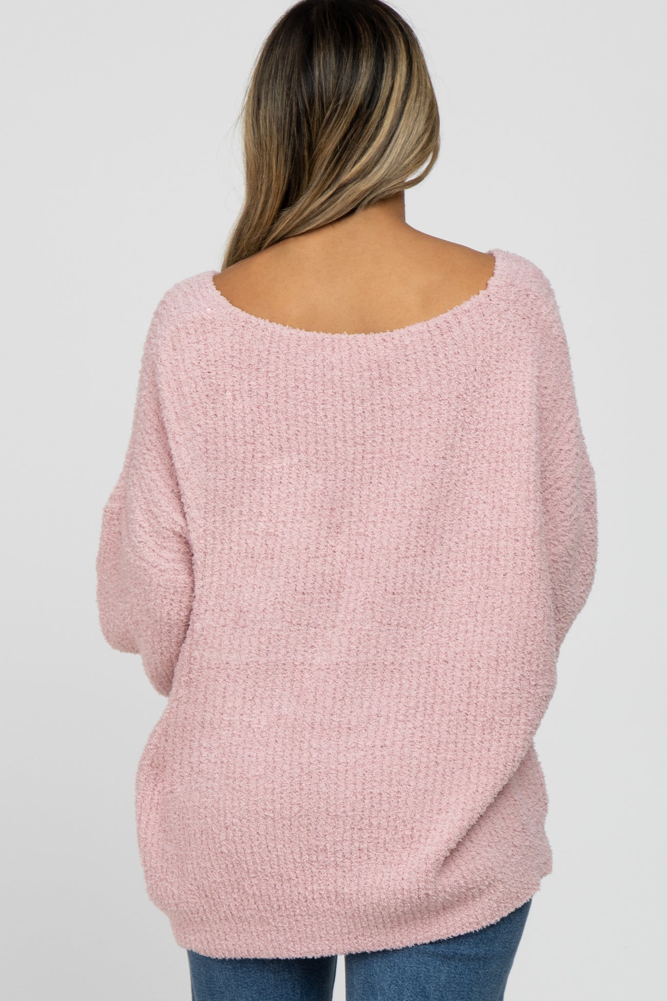 woman wearing a light pink oversized sweater with a wide neckline and long sleeves, seen from the back