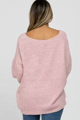 woman wearing a light pink oversized sweater with a wide neckline and long sleeves, seen from the back