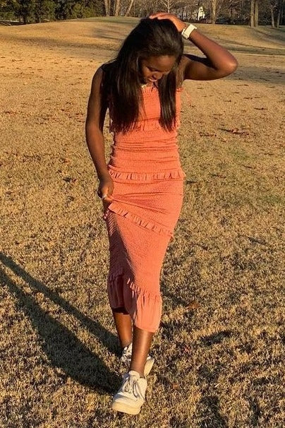 woman in orange smocked midi dress with ruffles posing in a grassy field at sunset