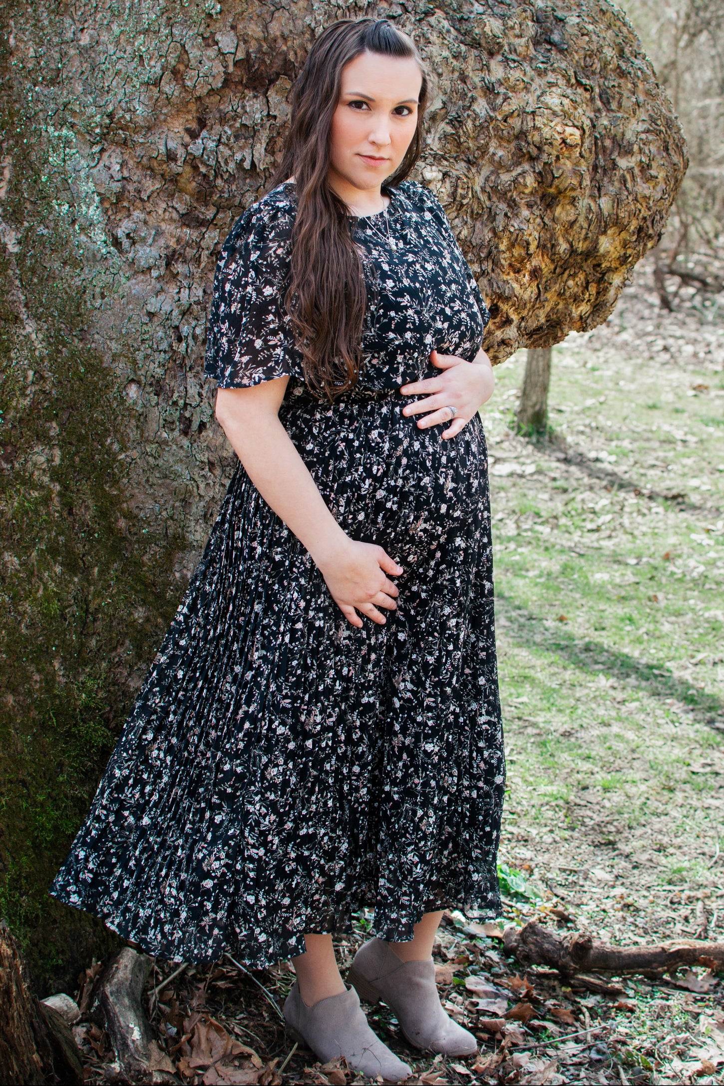 woman wearing a black floral print maternity maxi dress and holding her baby bump while posing outdoors