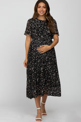 woman wearing a black floral print maternity dress with short sleeves and a flowing skirt, holding her baby bump