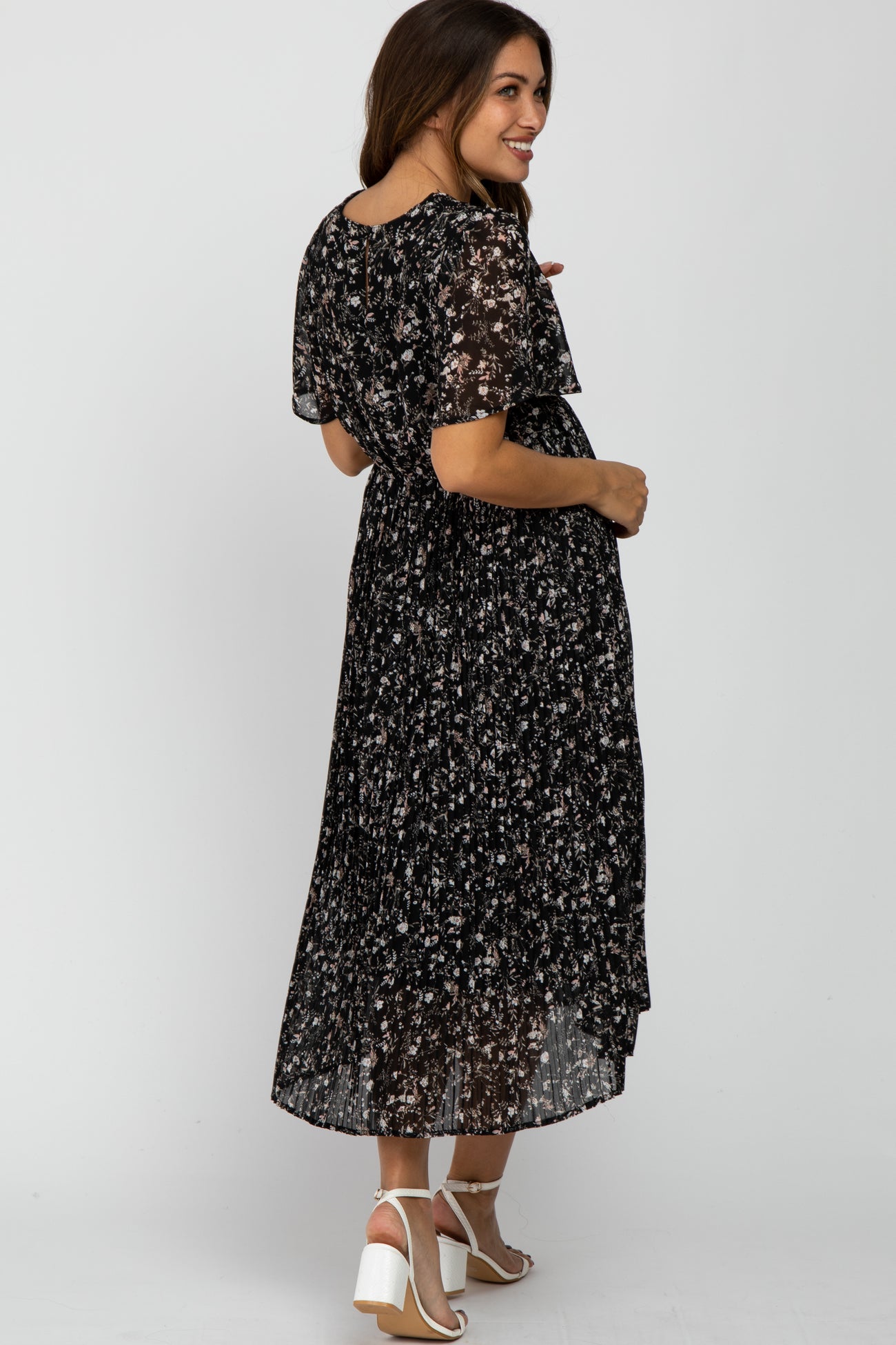 woman wearing a black floral maternity dress with short sleeves and a pleated skirt, showing her baby bump from the side