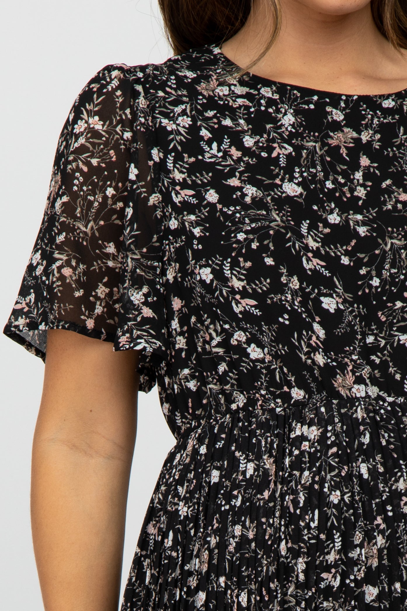 woman wearing a black floral print maternity dress with short flutter sleeves and a gathered waist