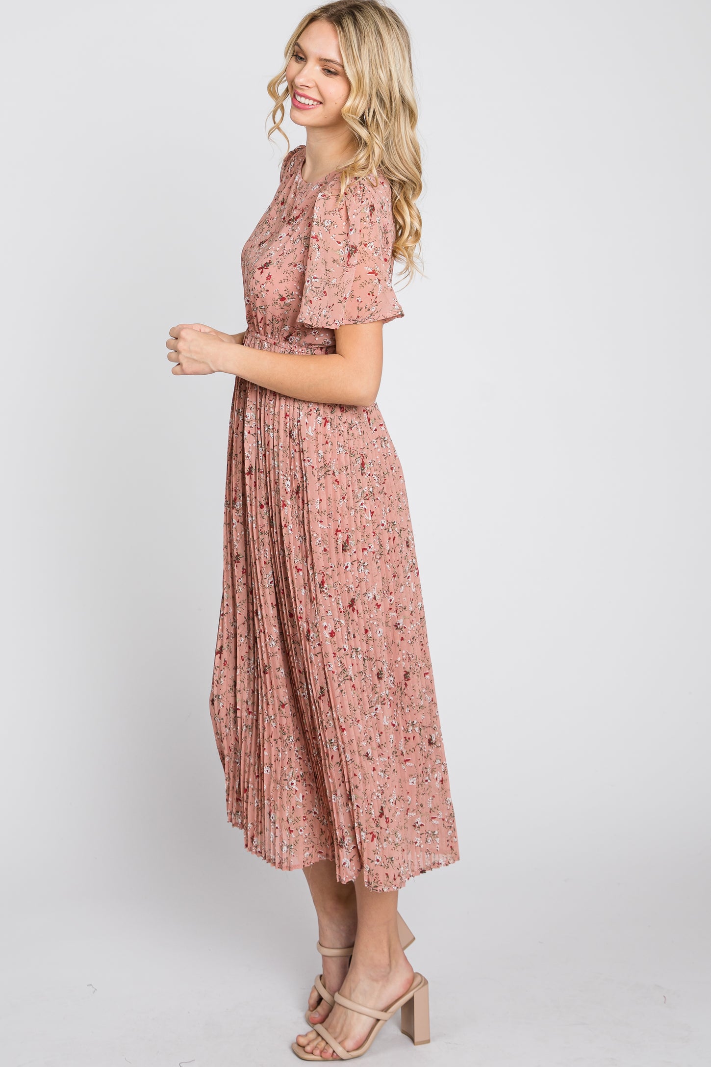 woman wearing a pink floral pleated midi dress with short sleeves and tan block heel sandals