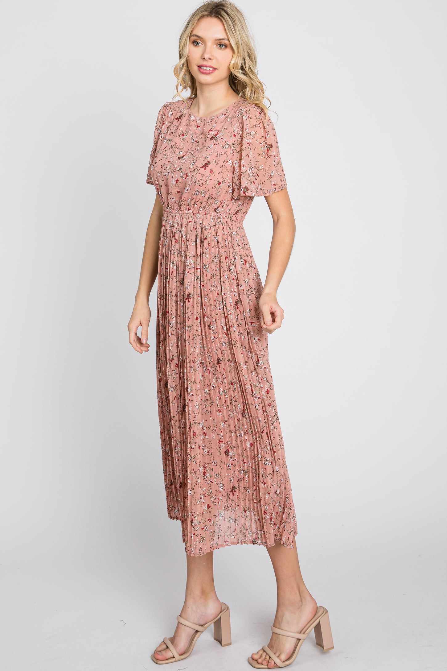 woman wearing a pink floral midi dress with short sleeves and pleated details, standing in a relaxed pose