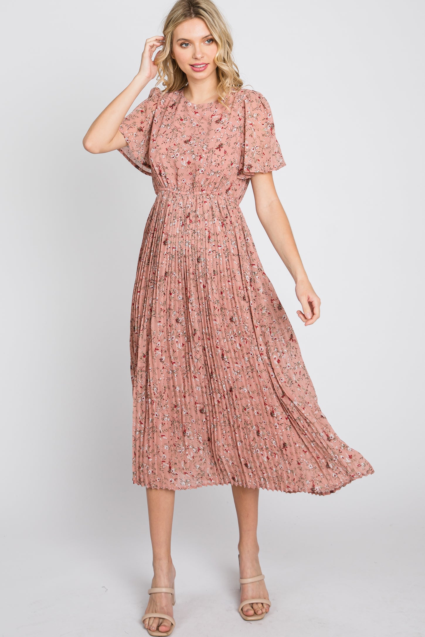 Woman wearing a pink floral midi dress with flutter sleeves and a pleated skirt against a white background