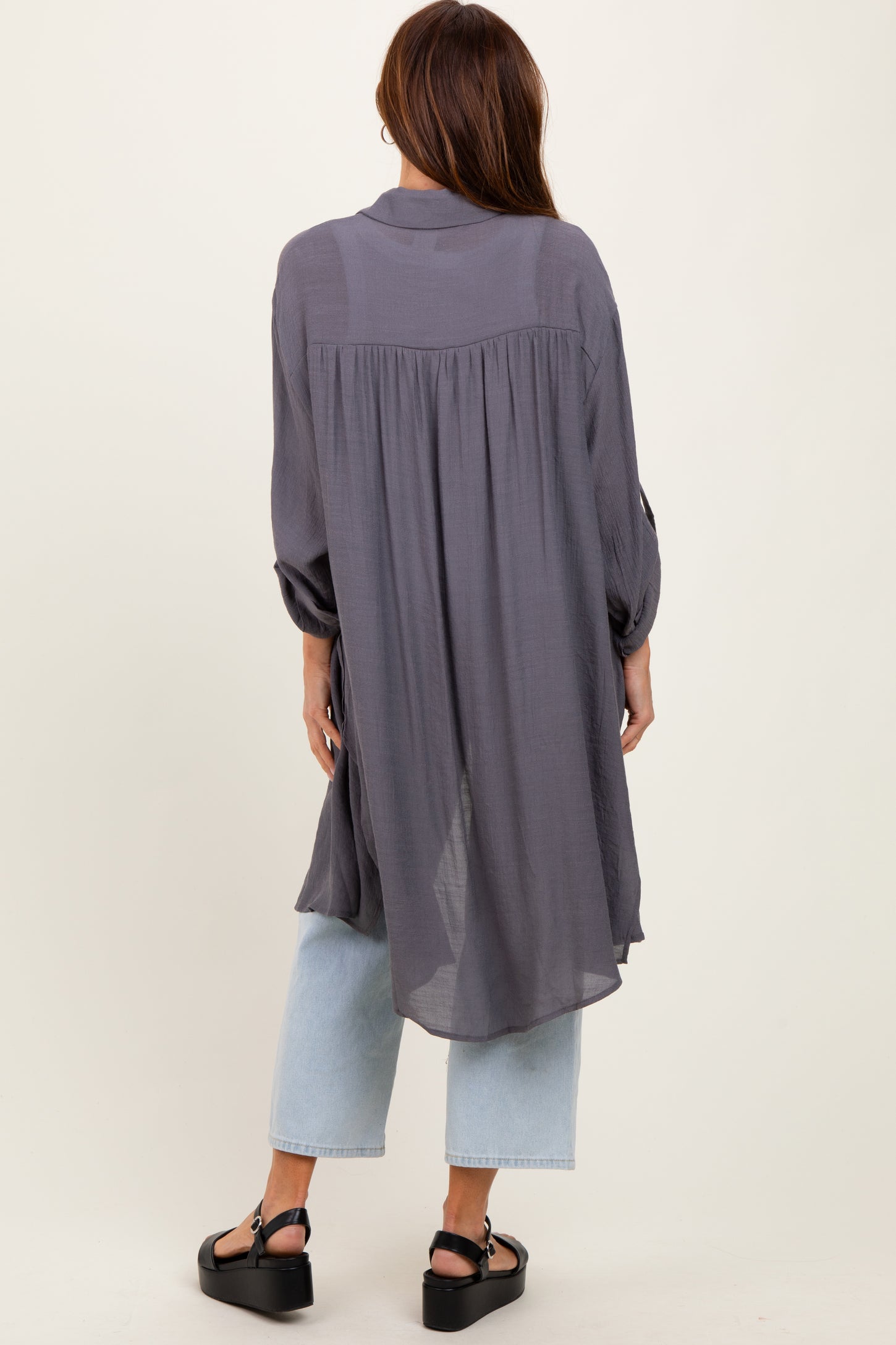 woman wearing a long gray button-up shirt with a flowy back, paired with light blue wide-leg jeans and black sandals