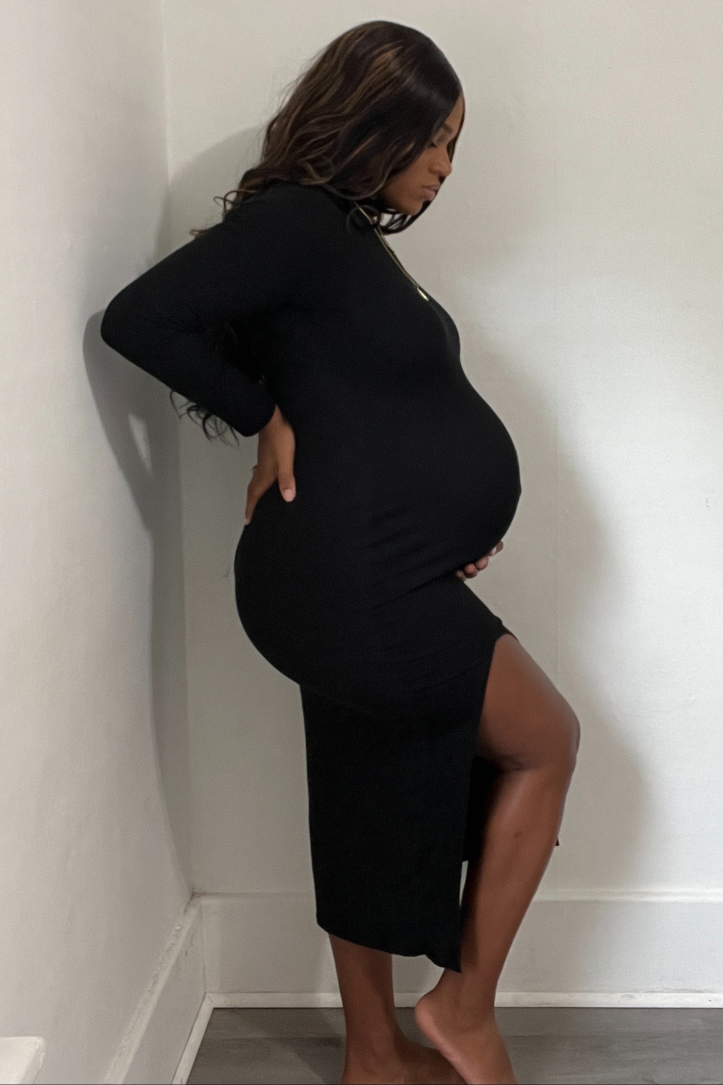 woman wearing a black long sleeve maternity dress with a side slit and visible baby bump