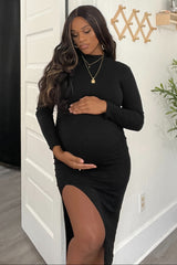 woman wearing a black maternity dress with a thigh-high slit and holding her baby bump