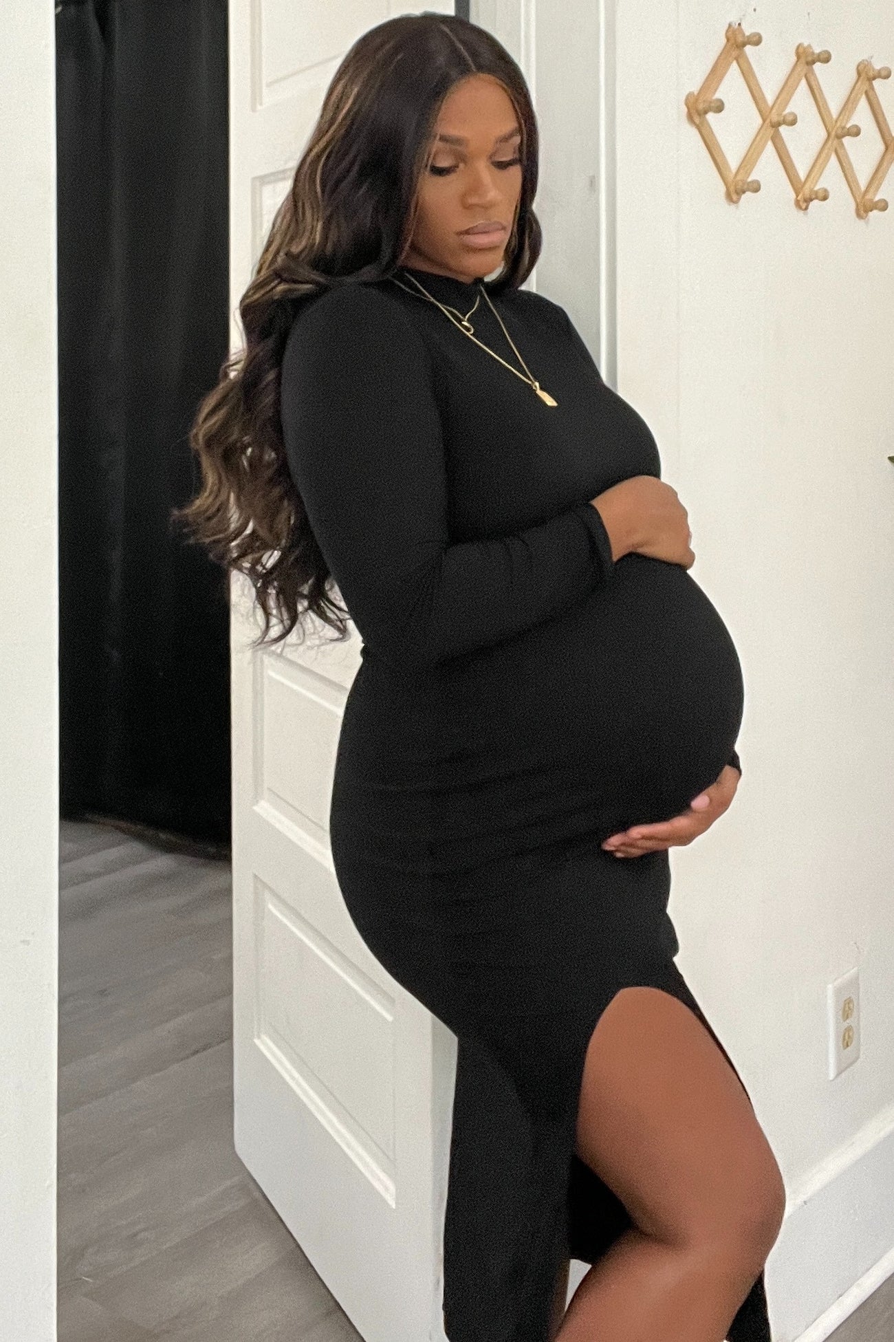 woman wearing a black long sleeve maternity dress with a side slit and holding her baby bump