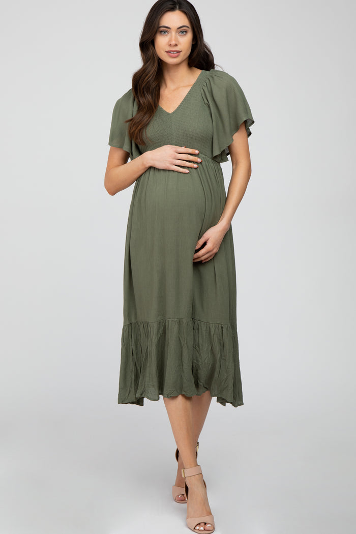 woman wearing an olive green maternity dress with flutter sleeves and a tiered hem, cradling her baby bump