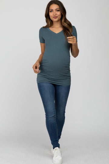 woman wearing a teal short sleeve maternity top that accentuates her baby bump and paired with skinny jeans