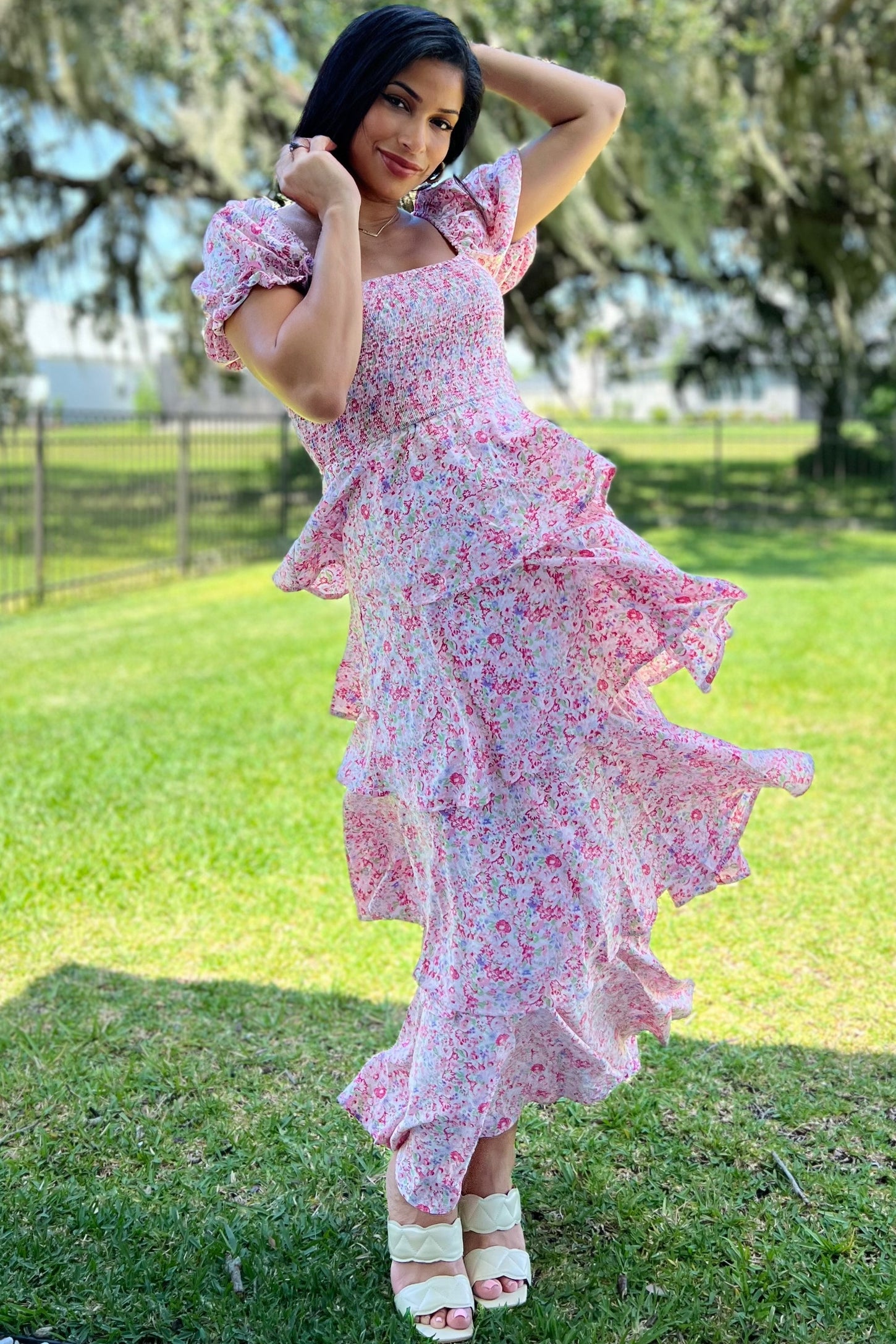 woman wearing a pink floral puff sleeve maxi dress with ruffles, standing on grass and smiling