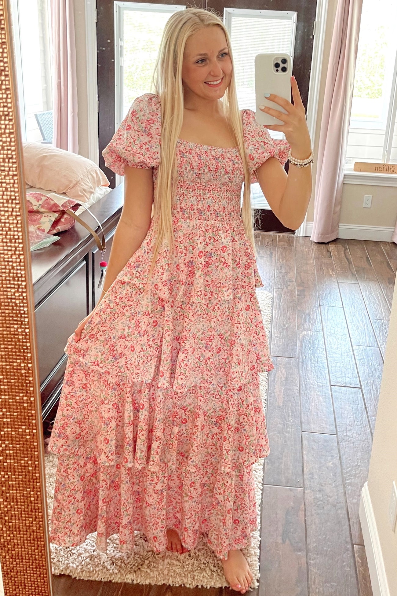 woman wearing a pink floral maxi dress with puff sleeves and tiered skirt, standing and smiling in front of a mirror