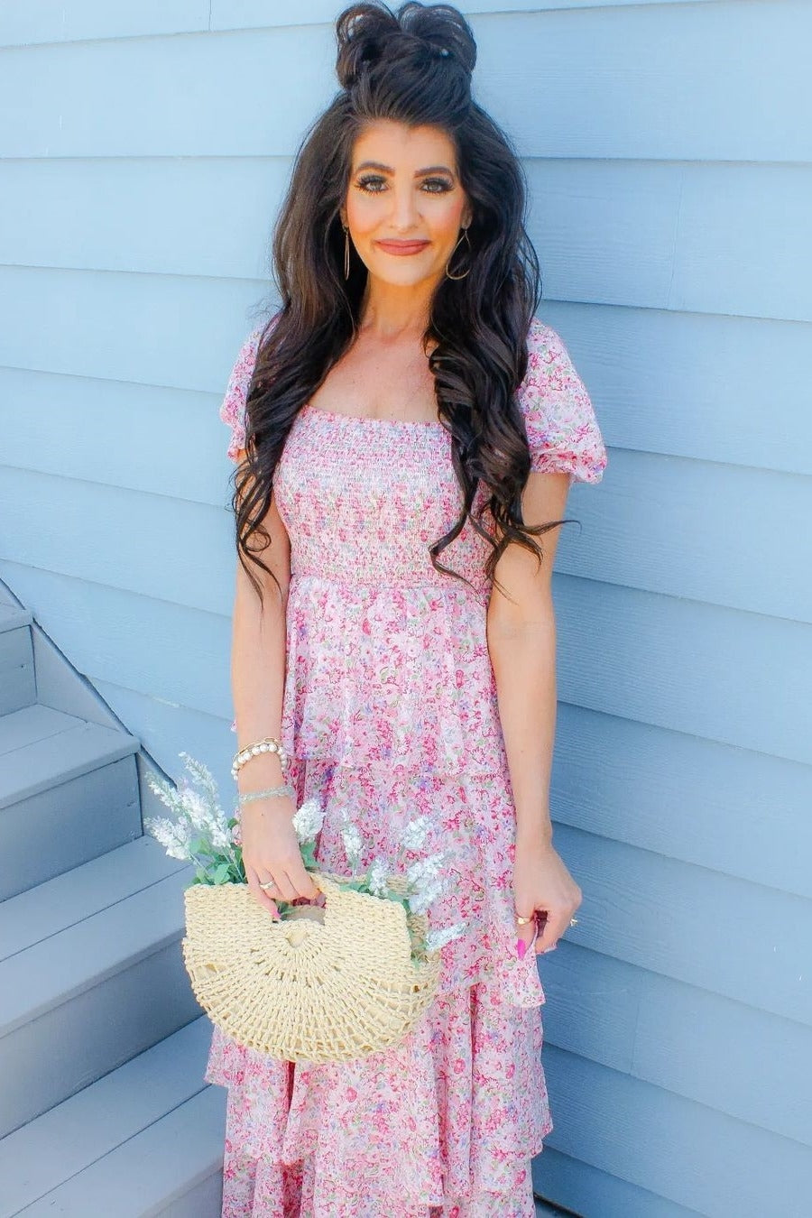 woman wearing a pink floral smocked maxi dress with puff sleeves and holding a straw bag with flowers