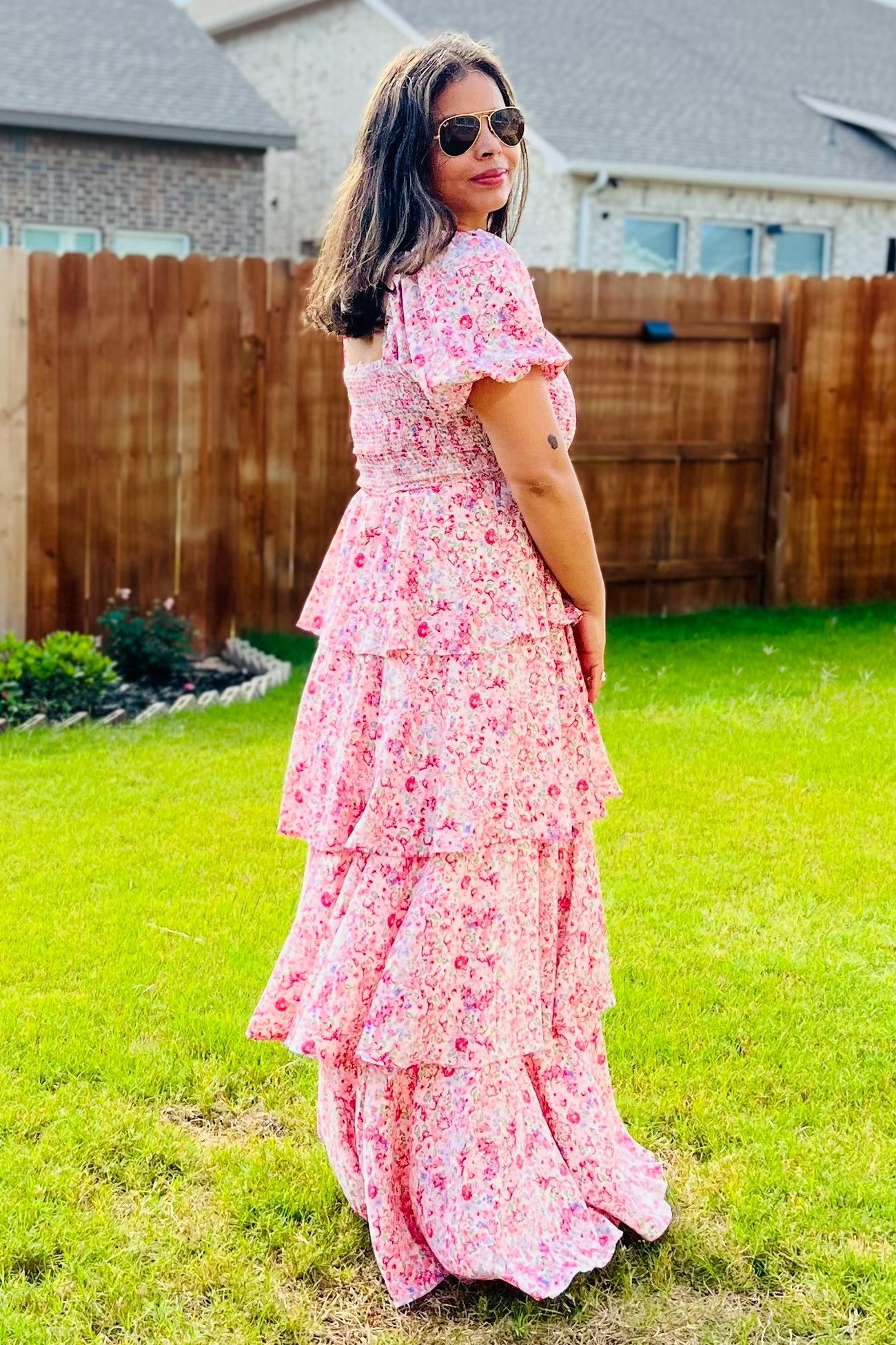 woman wearing a pink floral maxi dress with tiered ruffle details, standing in a garden with sunglasses on