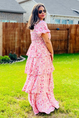woman wearing a pink floral maxi dress with tiered ruffle details, standing in a garden with sunglasses on