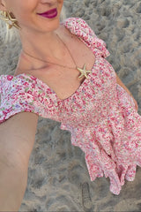 woman wearing a pink floral puff sleeve dress with a smocked bodice and starfish necklace, standing on the beach