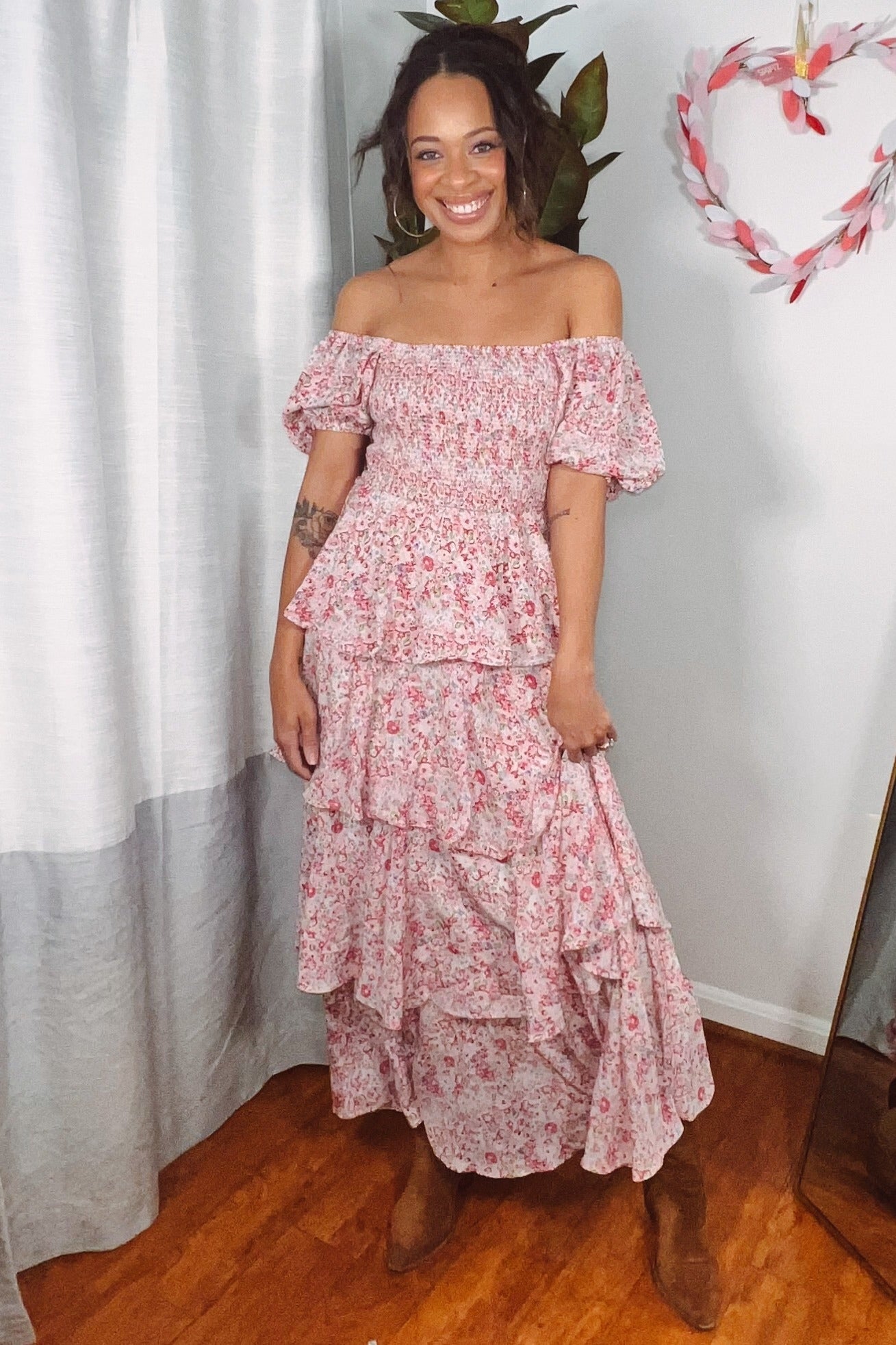 woman wearing a off-the-shoulder pink floral maxi dress with ruffled tiers and standing in a bright room
